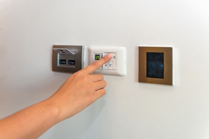 Image of someone touching an HVAC control panel. Heat Pump Versus Furnace.