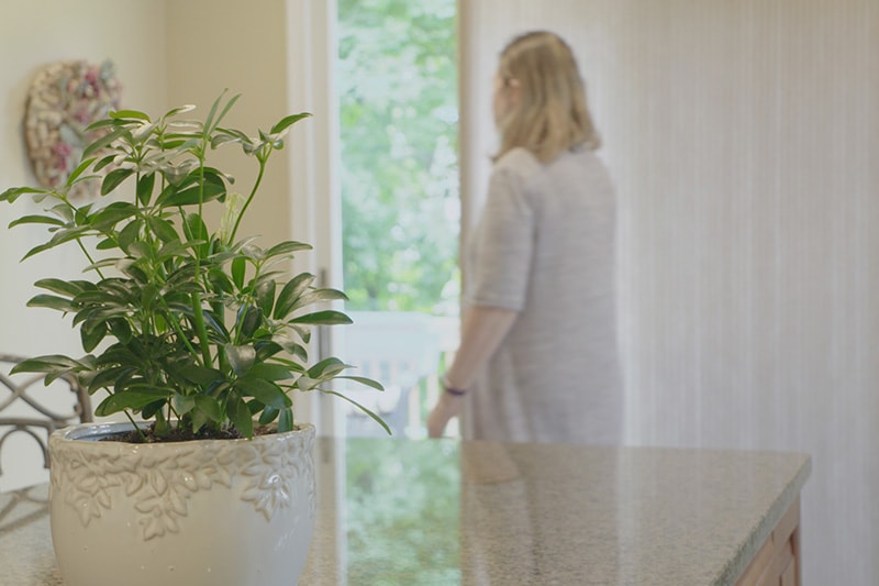 Video - Energy Saving Tip 3. Blonde woman opening a door with a large plant next to her.