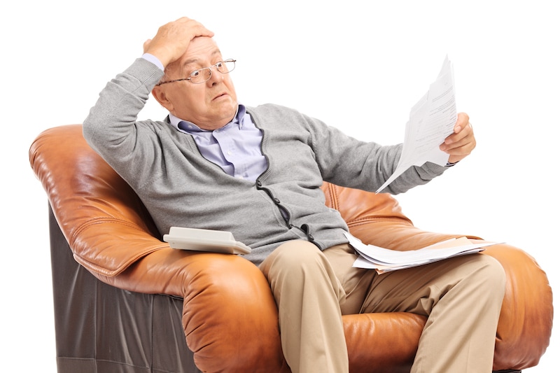 Shocked elderly man looks at his bills in disbelief.